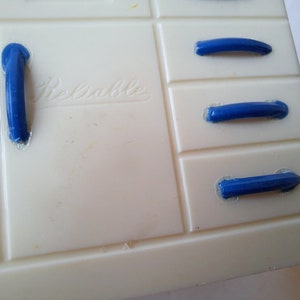 May include: White plastic toy kitchen cabinet with blue plastic drawer pulls. The cabinet has the word "Remarkable" printed on the front.