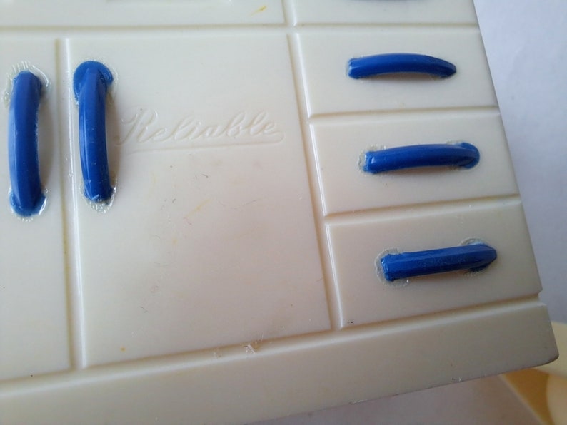 May include: White plastic toy kitchen cabinet with blue plastic drawer pulls. The cabinet has the word "Remarkable" printed on the front.