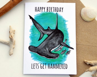 May include: A humorous birthday card featuring a cartoon hammerhead shark with the text "Happy Birthday" and "Let's Get Hammered".