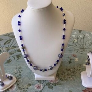 May include: A set of jewellery featuring a necklace, bracelet and earrings. The necklace and bracelet have blue and silver beads, while the earrings are silver with blue accents.