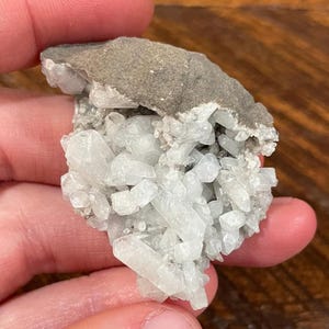 May include: A cluster of clear, crystalline formations with a light gray, rough matrix. The crystals are clustered together, creating a textured appearance. The overall color palette is a mix of gray and white.
