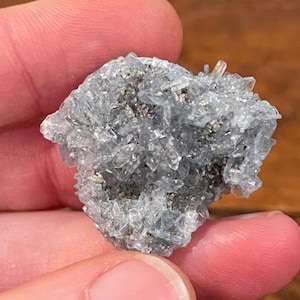 May include: A cluster of light blue celestite crystals. The crystals are small, translucent, and clustered together, with a few larger, more defined crystals at the top. The overall appearance is rough and natural, with a mix of light and dark blue hues.