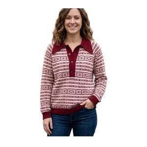 May include: A long-sleeved knit sweater featuring a light pink base with a repeating dark maroon geometric pattern. The garment includes a dark maroon pointed collar, a partial button-down placket with three visible buttons, and ribbed cuffs.