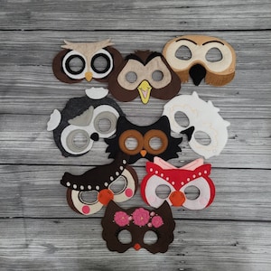 Op de afbeelding: Een verzameling handgemaakte uilenmaskers in verschillende kleuren en ontwerpen. De maskers zijn gemaakt van vilt en hebben verschillende oogvormen, snavels en decoratieve elementen. Sommige maskers hebben bloemaccenten of gedetailleerde patronen.