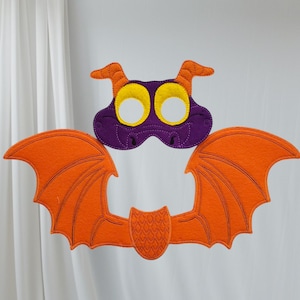 May include: A purple and orange felt dragon costume mask with wings. The mask has yellow eyes and a stitched mouth. The wings are attached to the mask with a felt strip.
