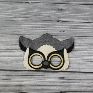 May include: A gray felt animal mask with black eyes and a yellow outline. The mask is shaped like a lemur with large ears.