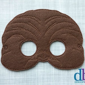 Könnte beinhalten: Braune Filzmaske mit zwei Augenlöchern und einem gestickten Design, das einem Gesicht ähnelt. Die Maske ist für ein Kind und hat eine braune Filzrückseite.