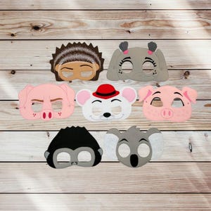 May include: A collection of seven felt animal masks including a brown hedgehog, a gray elephant, two pink pigs, a white mouse with a red hat, a black monkey, and a gray koala. Each mask features cutouts for eyes and detailed stitched facial features.