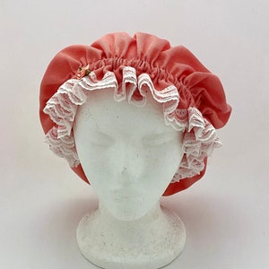 May include: A coral pink shower cap with white lace trim and a small pink flower embellishment.