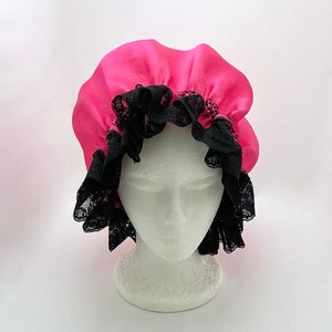 May include: A pink satin shower cap with black lace trim. The cap is on a white mannequin head.