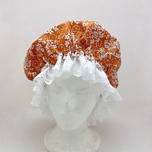 May include: A white and orange shower cap with a white lace trim. The cap is made of satin and has a floral pattern.