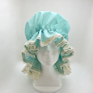 May include: A light blue fabric shower cap with white lace trim. The cap is gathered at the top and has a ruffled edge.