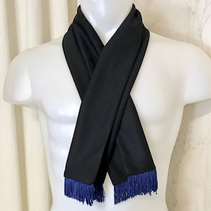 May include: A black scarf with blue fringe on the ends. The scarf is folded and displayed on a white mannequin.