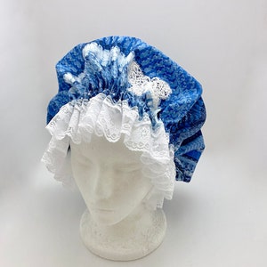 May include: A blue and white patterned shower cap with white lace trim. The cap is on a white mannequin head.