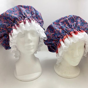 May include: Two floral print shower caps with white lace trim and pink elastic bands. The caps are on white mannequin heads.