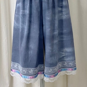May include: Gray cotton shorts with a white lace trim and a colorful ribbon trim. The shorts have a faded, watercolor-like design.