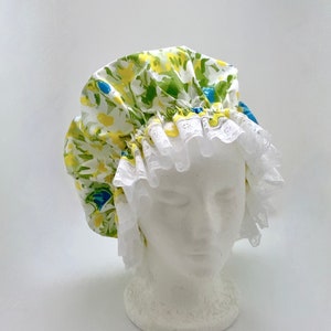 May include: A white shower cap with a green, yellow, and blue floral print and white lace trim.