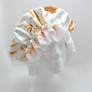 May include: A white shower cap with a lace trim and a floral print in shades of orange and brown.