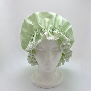 May include: A light green satin shower cap with white lace trim. The cap is gathered at the top and has a ruffled edge.