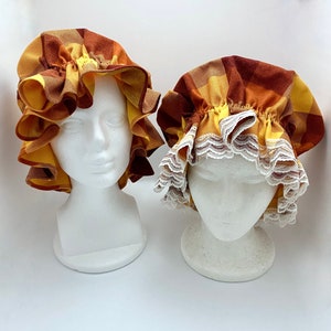 May include: Two yellow and orange ruffled fabric caps with white lace trim. The caps are on white mannequin heads.