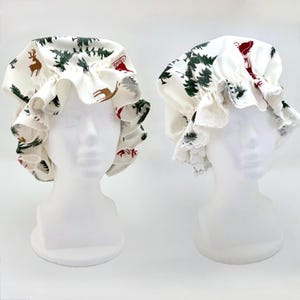 May include: Two white shower caps with a festive Christmas print featuring reindeer, trees, and a sleigh. The caps have a ruffled edge and are displayed on white mannequin heads, perfect for holiday gifting or personal use.