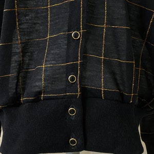 May include: Black cardigan with a gold checkered pattern and gold button closures.