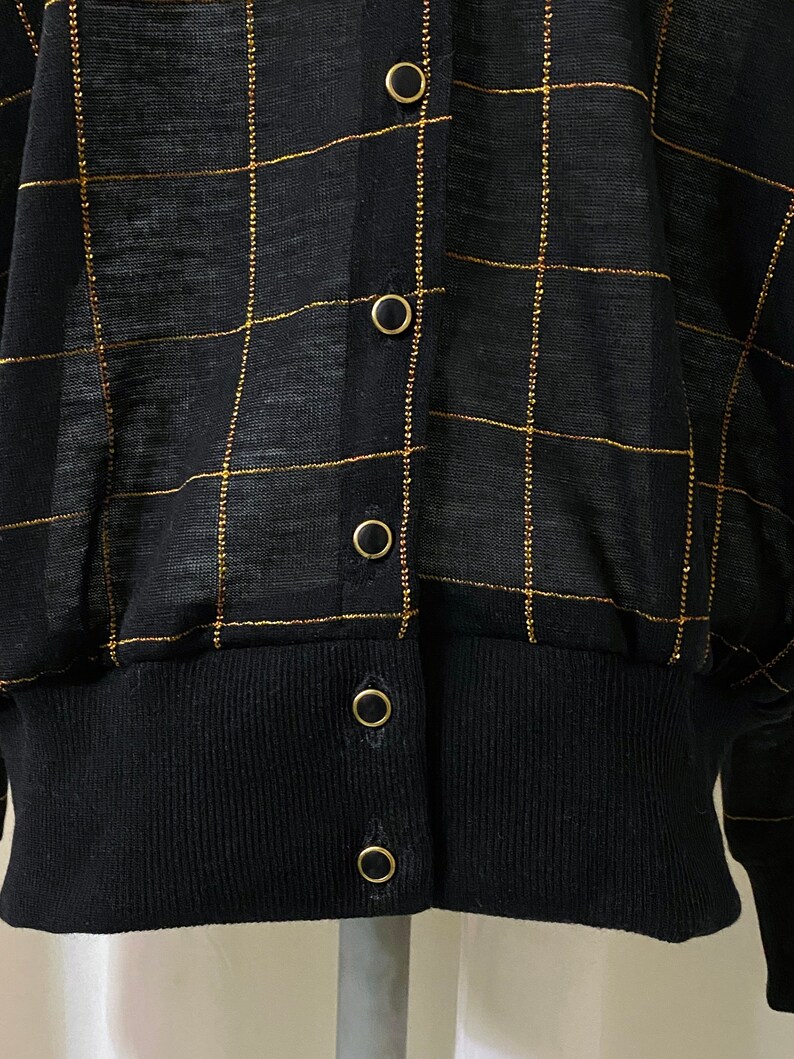 May include: Black cardigan with a gold checkered pattern and gold button closures.