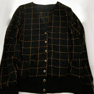 May include: Black cardigan with a gold grid pattern and button closure.