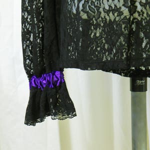 May include: Black lace top with a purple ribbon detail on the sleeve. The top is sheer and has a delicate floral pattern.