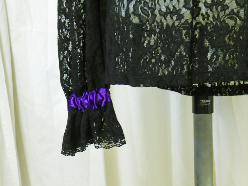 May include: Black lace top with a purple ribbon detail on the sleeve. The top is sheer and has a delicate floral pattern.