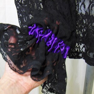 May include: Black lace fabric with a purple satin ribbon trim. The lace has a delicate floral pattern.