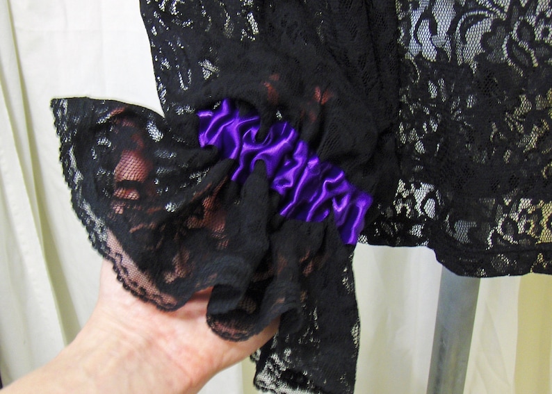 May include: Black lace fabric with a purple satin ribbon trim. The lace has a delicate floral pattern.