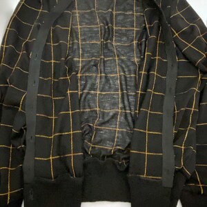 May include: Black cardigan with gold grid pattern and black buttons. The cardigan is open and the inside is visible.