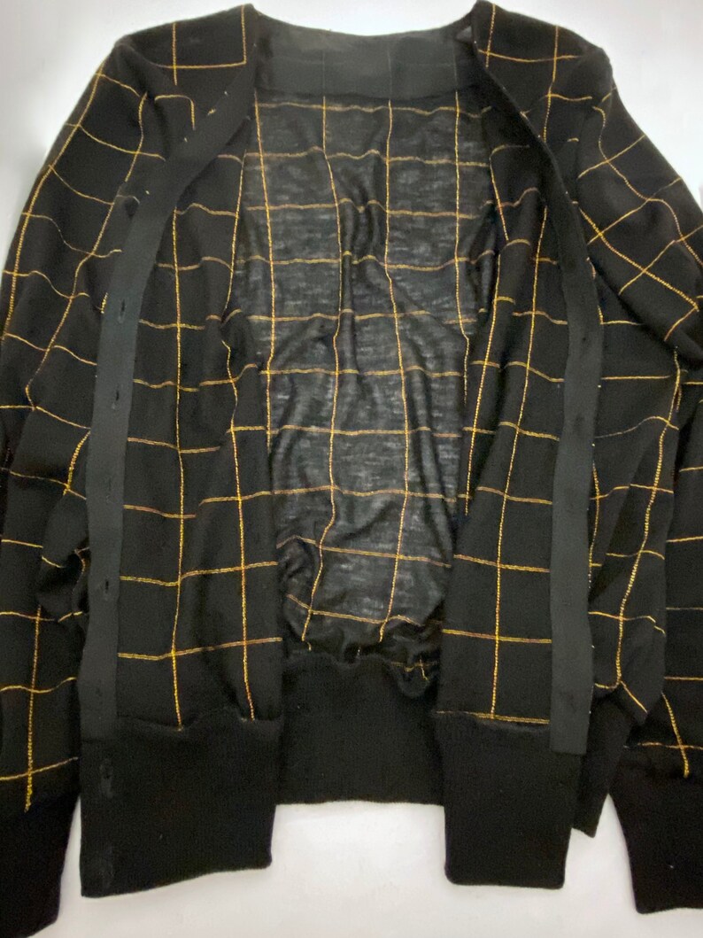 May include: Black cardigan with gold grid pattern and black buttons. The cardigan is open and the inside is visible.