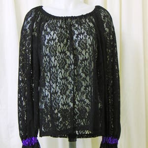 May include: Black lace blouse with long sleeves and a gathered neckline. The sleeves have ruffled cuffs with purple ribbon trim.