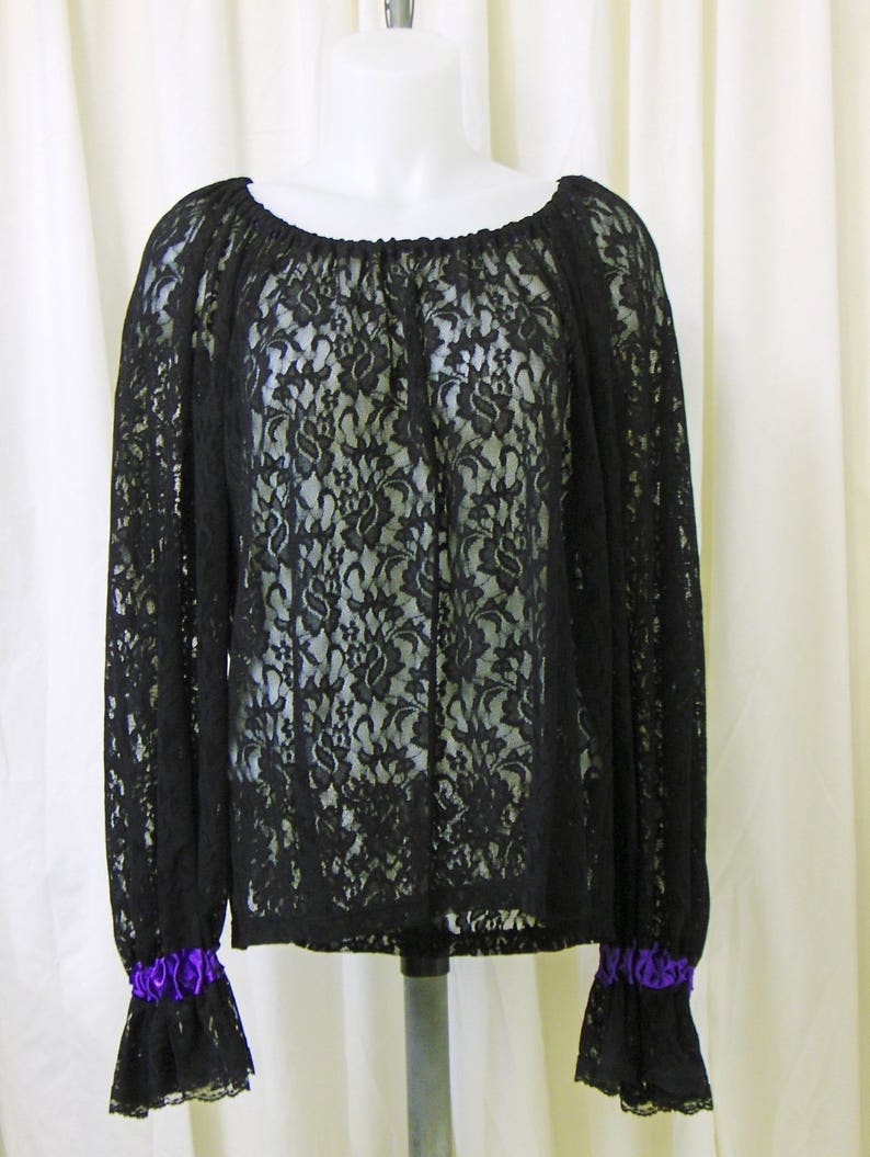 May include: Black lace blouse with long sleeves and a gathered neckline. The sleeves have ruffled cuffs with purple ribbon trim.