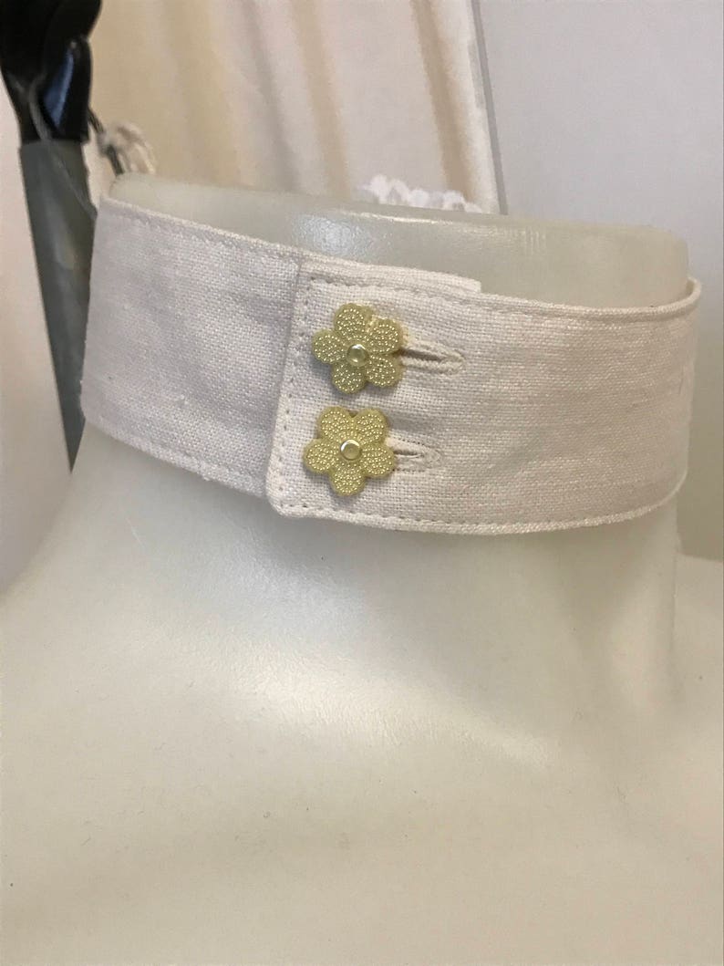 Puede incluir: Un cuello de lino blanco con dos botones dorados en forma de flor.