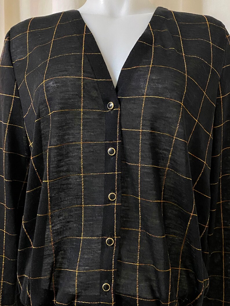 May include: A black long-sleeved button-up shirt with a gold grid pattern.
