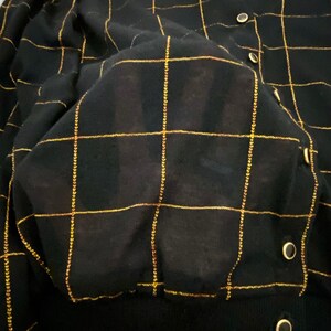 May include: Black cardigan with a gold grid pattern. The cardigan has a button closure and a ribbed texture.