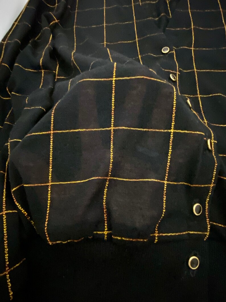 May include: Black cardigan with a gold grid pattern. The cardigan has a button closure and a ribbed texture.