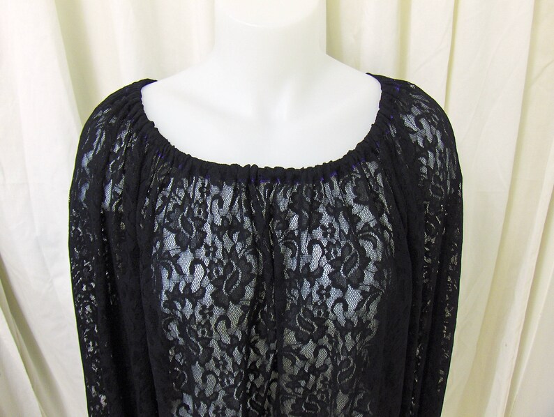 May include: Black lace top with a wide, gathered neckline. The top is sheer and has a delicate floral pattern.