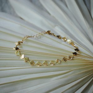 May include: A gold chain bracelet with a delicate design featuring a series of small, scalloped shell-shaped charms.