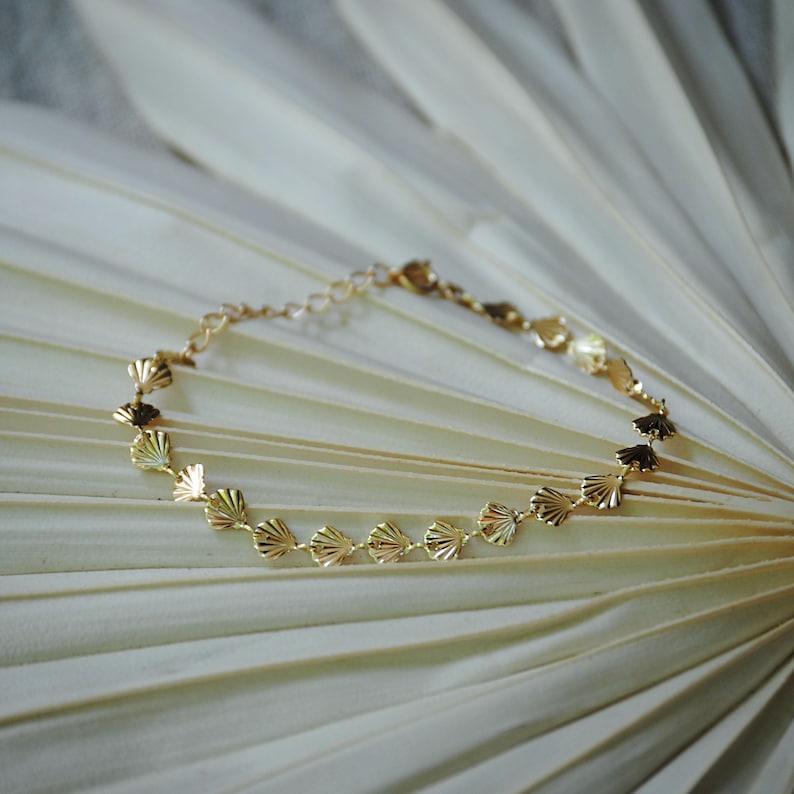 May include: A gold chain bracelet with a delicate design featuring a series of small, scalloped shell-shaped charms.