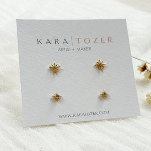 May include: Four pairs of gold-colored starburst stud earrings on a white card. The card has the text "KARA TOZER ARTIST + MAKER" and the website address www.karatozer.com.