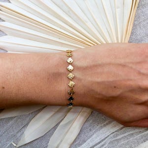 May include: A gold bracelet with a delicate chain and small, scallop-shaped charms. The bracelet is on a person's wrist.
