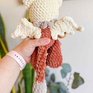 May include: A handmade crochet angel doll with cream-colored head and wings, a rust-colored body, and a gray tail. The doll has a textured, plush appearance and a small brown pom-pom on top of its head.