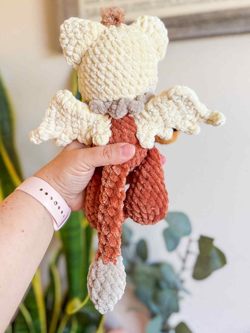 May include: A handmade crochet angel doll with cream-colored head and wings, a rust-colored body, and a gray tail. The doll has a textured, plush appearance and a small brown pom-pom on top of its head.