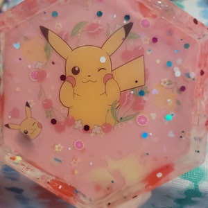 May include: A hexagonal resin tray with a pink background, featuring a cheerful Pikachu design surrounded by flowers, cherries, and glitter. The tray has a clear, glossy finish and is suitable for holding small items.
