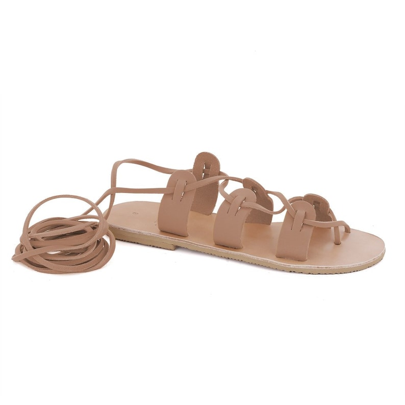 May include: Tan leather sandals with multiple straps and laces that tie up the leg. The sandals have a flat sole.