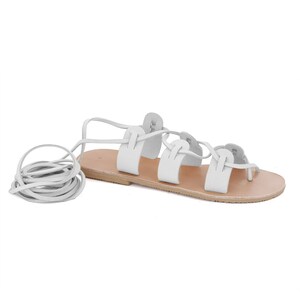 May include: White leather sandals with a lace-up design. The laces are tied around the ankle and foot, and the sandals have a flat sole.